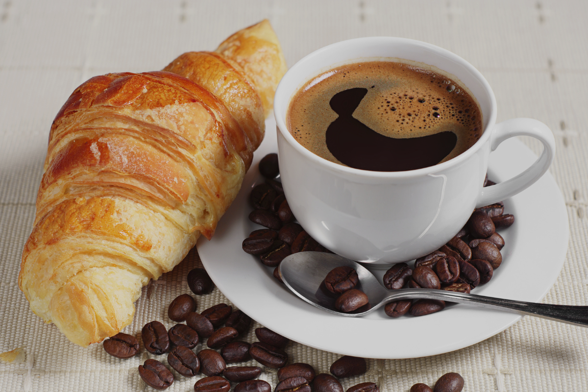 a cup of coffee surrounded by coffee beans and a croissant