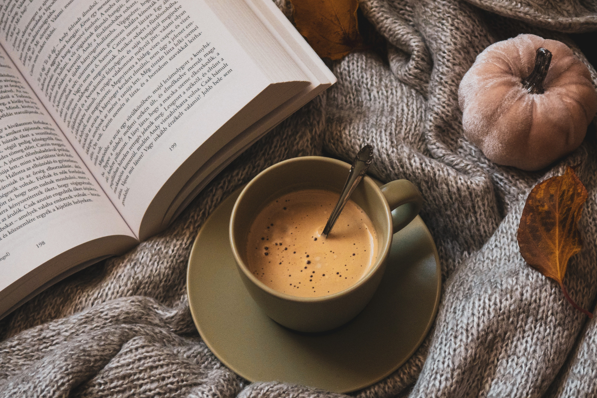 Coffee in a bed next to a book and some autumn themed decorations